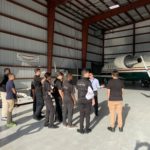 Students welcomed at hangar with corporate jet in background.
