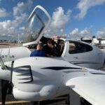 Lynn University student pilot and instructor seated in Diamond Twin Star multi-engine plane as one student stands outside.