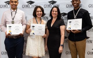 4 people standing in front of a photo wall for The George Snow Scholarship